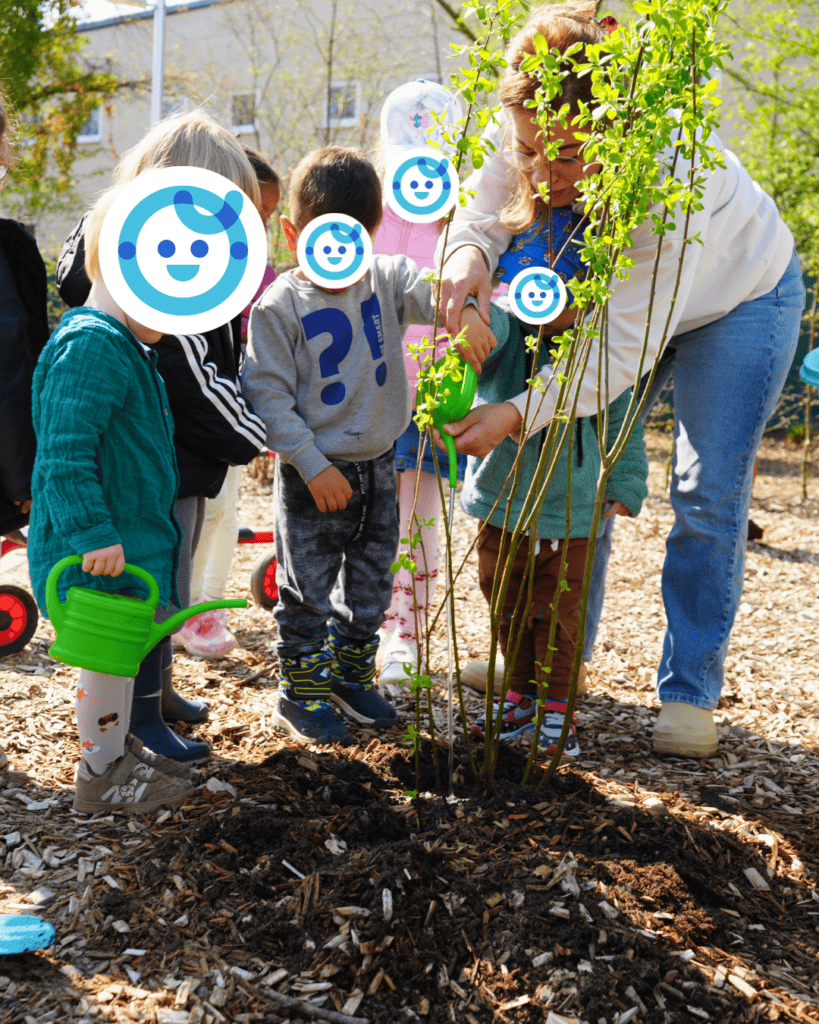 Eine Gruppe Kinder pflanzt mit einer Erzieherin zusammen eine Sal Weide in einem Beet.