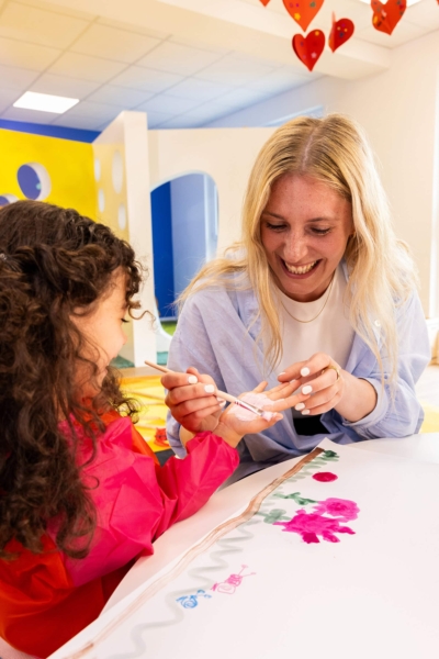 Pädagogin die einem Kind Fingerfarbe aufrägt in der Kita kinderzimmer Hamburg