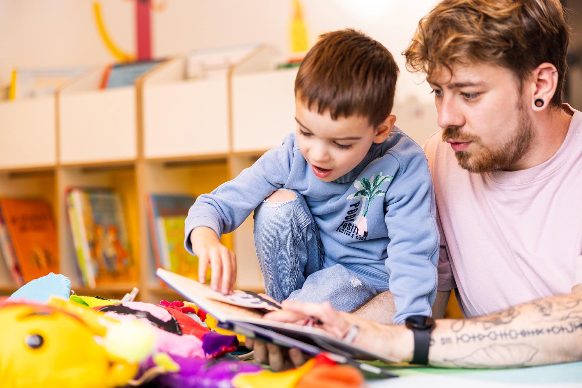 kita-kinderzimmer-hamburg-brand-shooting-kjell-kind-3x7a4230 Ein Erzieher und ein Kind lesen zusammen ein Buch in der Kita kinderzimmer Hamburg