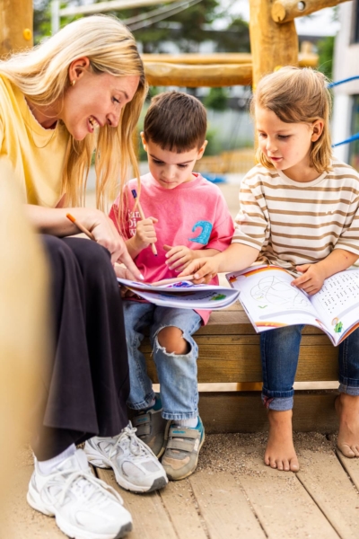 vorschule-kita-kinderzimmer-hamburg-kita-motiv-3X7A7096 Zwei Vorschulkinder aus der Kita kinderzimmer Hamburg lösen gemeinsam mit einer Erzieherin auf einem Klettergerüst Vorschulaufgaben aus einem Heft