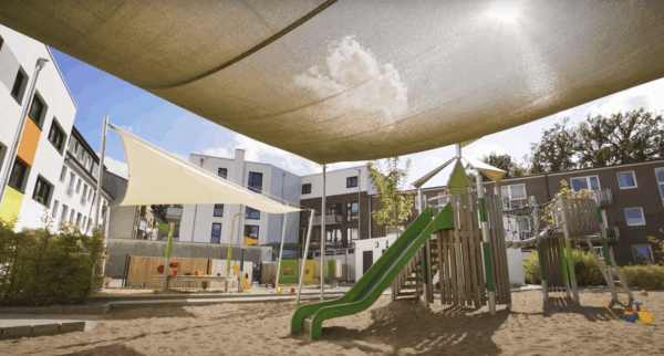 Spielplatz im Kinderzimmer der Kita Spielplatz mit Rutsche und Schatten spendendem Sonnensegel.