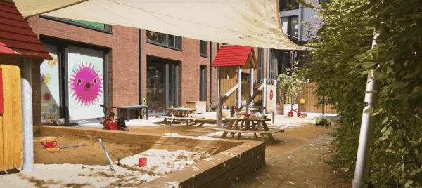 kita-kinderzimmer-lohsepark-hamburg-hafen-city-außen-4 Sandkasten im Kita-Garten mit Spielgeräten und Schatten spendendem Sonnensegel.