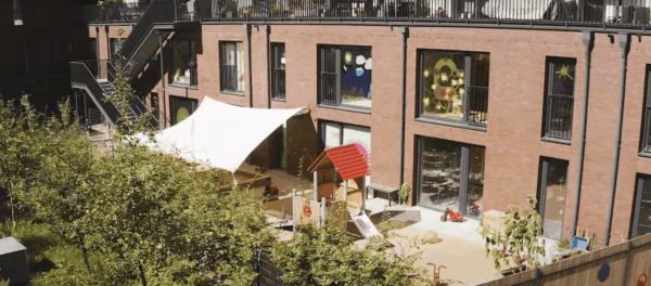 kita-kinderzimmer-lohsepark-hamburg-hafen-city-außen Kleiner Spielplatz im Innenhof der Kita mit Spielhaus und Klettergerüst.