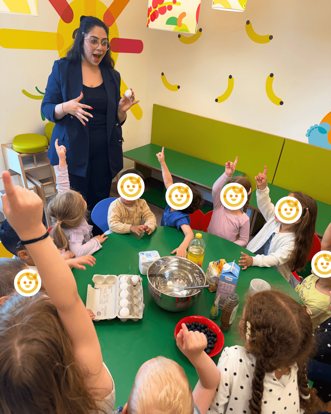 kita-kinderzimmer-hamburg-backen Eine Erzieherin backt mit einer Gruppe Kinder im Kinderrestaurant an einem grünen großen Tisch einen Kuchen in der Kita kinderzimmer Hamburg