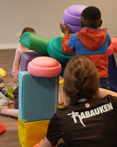 kita-kinderzimmer-hamburg-kooperation-rabauken2 Eine Trainerin der Sankt Pauli Rabauken baut mit einem Kind einen. Bewegungsparcours in der Kita kinderzimmer Hamburg
